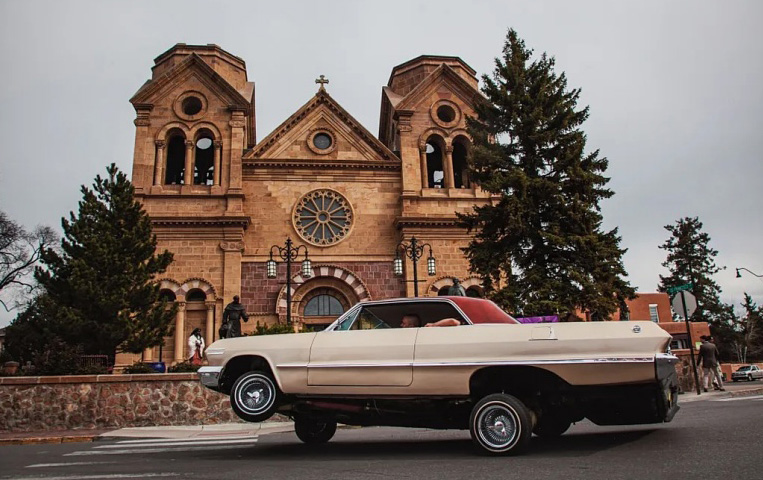Yellow low rider sedan with a red top shows off its hydraulics in front of a church.